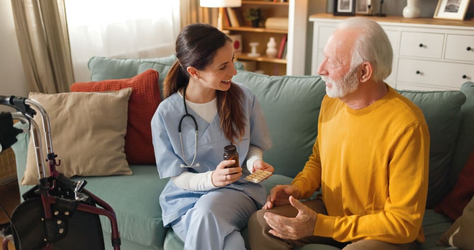 A home health nurse sitting with an older man in his living room during a visit